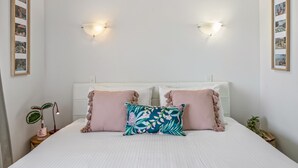 A neatly arranged bedroom with a bed, two bedside lamps, a nightstand with a plant, and framed pictures on the walls. - Great Location 1-bed With Pool (Sunshine Coast)