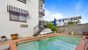 A swimming pool with a brick border, a staircase leading to an upper level, and potted plants around the area. - Great Location 1-bed With Pool (Sunshine Coast)