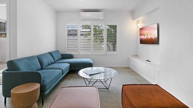 Ein modernes Wohnzimmer mit einem blauen Sofa, einem Glastisch und einem braunen Hocker.