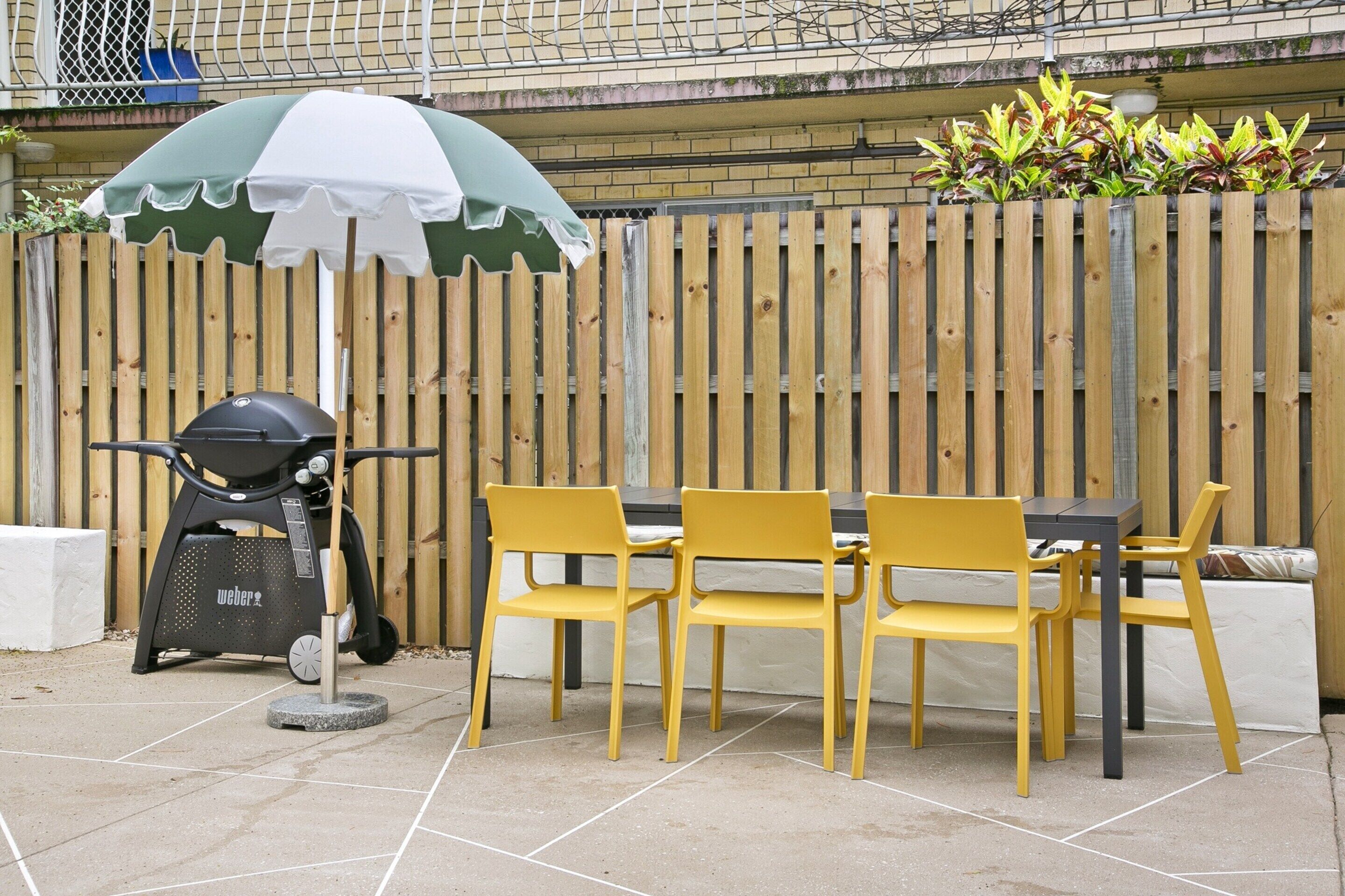 Patio esterno con griglia, sedie gialle e tavolo.