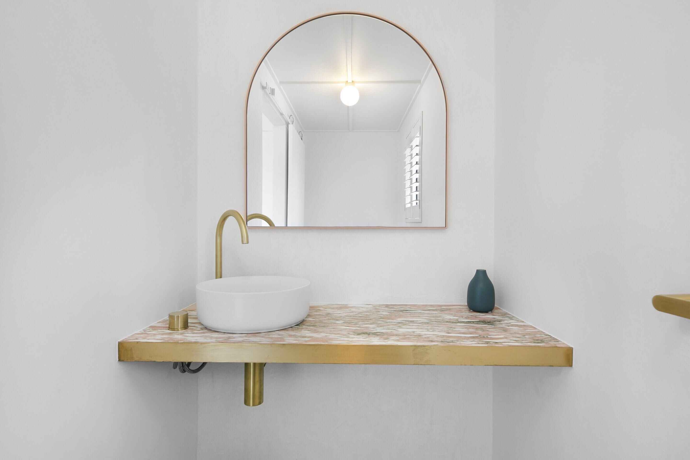 Ein Badezimmer mit einem weißen Waschbecken, einem goldfarbenen Wasserhahn und einem Spiegel mit goldener Rahmung.