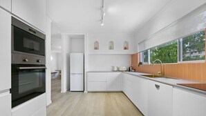 Eine moderne Küche mit weißen Schränken, einem Edelstahlbackofen, einem integrierten Kühlschrank und einem Fenster mit Blick auf Grünflächen.