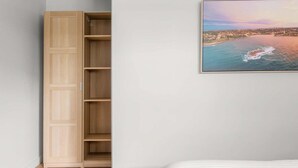 A bedroom with a bed, a wooden wardrobe, and a framed coastal landscape painting on the wall.