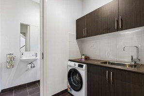 A compact laundry room with a washing machine, a sink, and dark wooden cabinets.
