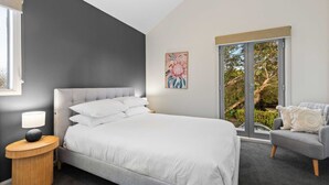 A modern bedroom with a large bed, a bedside table, a chair, and a window with a view of greenery. - Chic 2-bed Home By Bustling Shops (Melbourne)