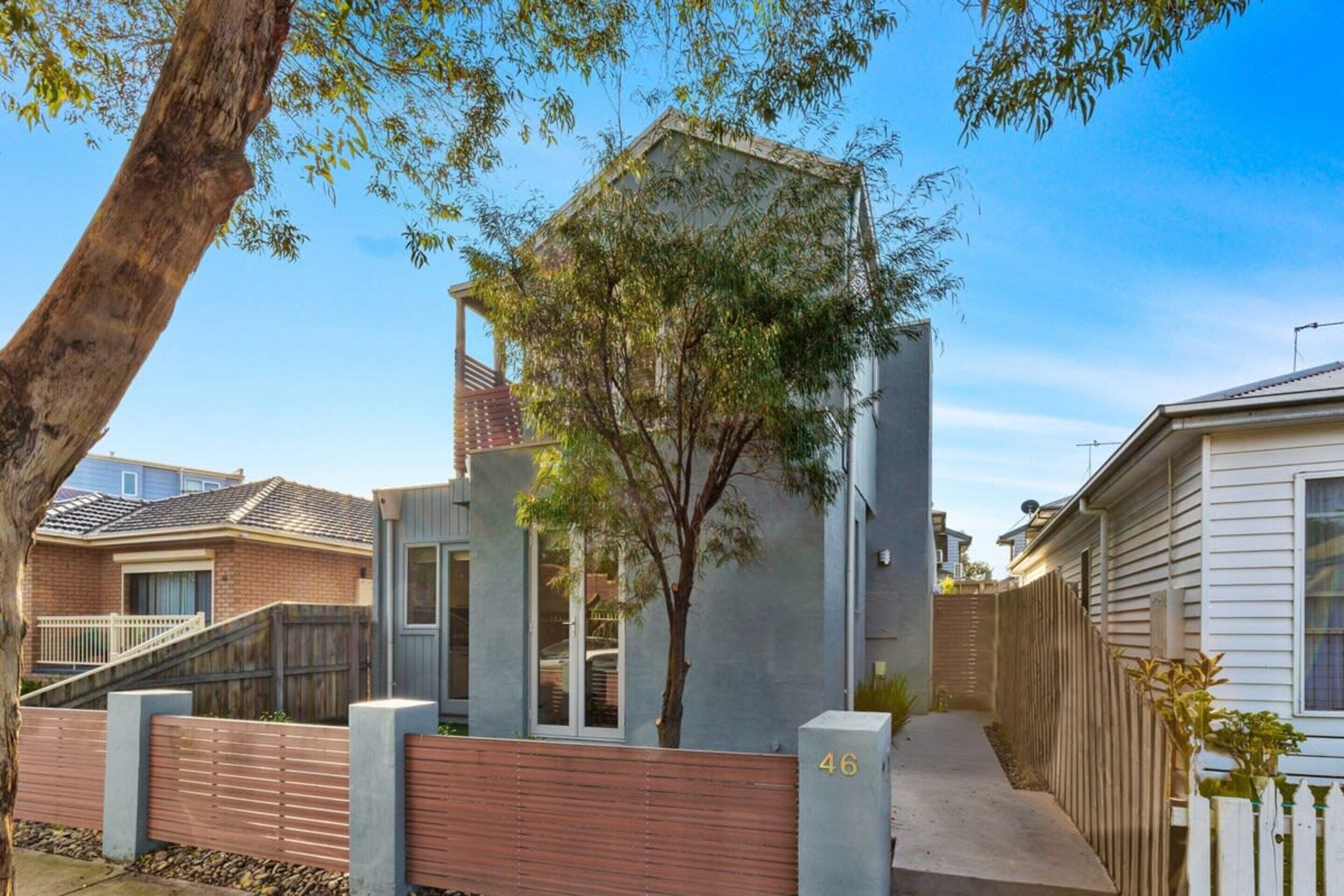 A residential property with a modern design, featuring a prominent tree in the center, a gated entrance, and a visible house number.