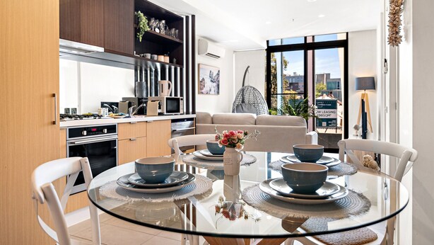 A modern kitchen with dark wood cabinets, a built-in oven, and a dining area with a glass table and white chairs. - Modern 2-bedroom Retreat Minutes From St Kilda (Melbourne)