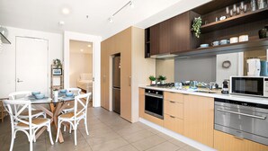 A modern kitchen with wooden cabinets, stainless steel appliances, and a dining area with white chairs. - Modern 2-bedroom Retreat Minutes From St Kilda (Melbourne)