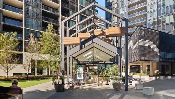 A modern building with a glass facade, a covered outdoor seating area, and a sign for 'Society Coffee Co.' - Sleek 2-bed Apartment With Rooftop Garden Access (Canberra)