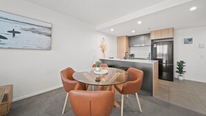 A modern kitchen with a central island, a dining area with a glass table and leather chairs, and a large painting on the wall. - Sleek 2-bed Apartment With Rooftop Garden Access (Canberra)