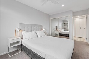 A bedroom with a large bed, a bedside table, a nightstand, a wardrobe, and a ceiling fan. - Sleek Kensington 2-bed With BBQ Area & Gym (Melbourne)