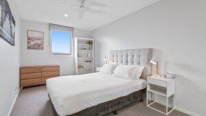 A bedroom with a bed, a nightstand, a bookshelf, a ceiling fan, and a window. - Sleek Kensington 2-bed With BBQ Area & Gym (Melbourne)