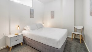 Ein ordentlich eingerichtetes Schlafzimmer mit Bett, Nachttisch, Lampe und Stuhl.