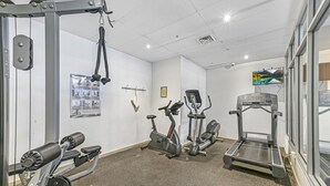 Ein Fitnessraum mit unterschiedlichen Trainingsgeräten, einem Wandfernseher und einem Poster.