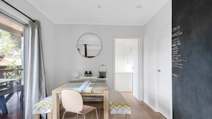 A dining area with a table, chairs, a mirror, and a chalkboard wall. - Cosy Getaway With Fireplace and Spacious Backyard (Broulee)