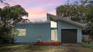 A modern house with a garage, a wooden front porch, and a large window. - Cosy Getaway With Fireplace and Spacious Backyard (Broulee)