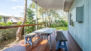 A covered patio with a wooden table and benches, surrounded by a wooden fence and trees. - Cosy Getaway With Fireplace and Spacious Backyard (Broulee)