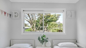 Une chambre avec deux lits, une fenêtre donnant sur des arbres et un parc, et une petite table avec un vase et une plante.