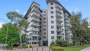 A modern multi-story residential building with balconies, a landscaped entrance area, and a clear sky. - Central Braddon Retreat With Balcony & Pool Access (Canberra)