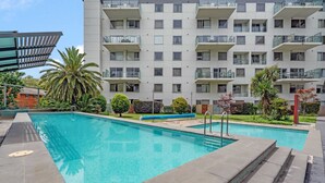 A modern apartment building with a swimming pool, surrounded by well-maintained greenery and palm trees. - Central Braddon Retreat With Balcony & Pool Access (Canberra)