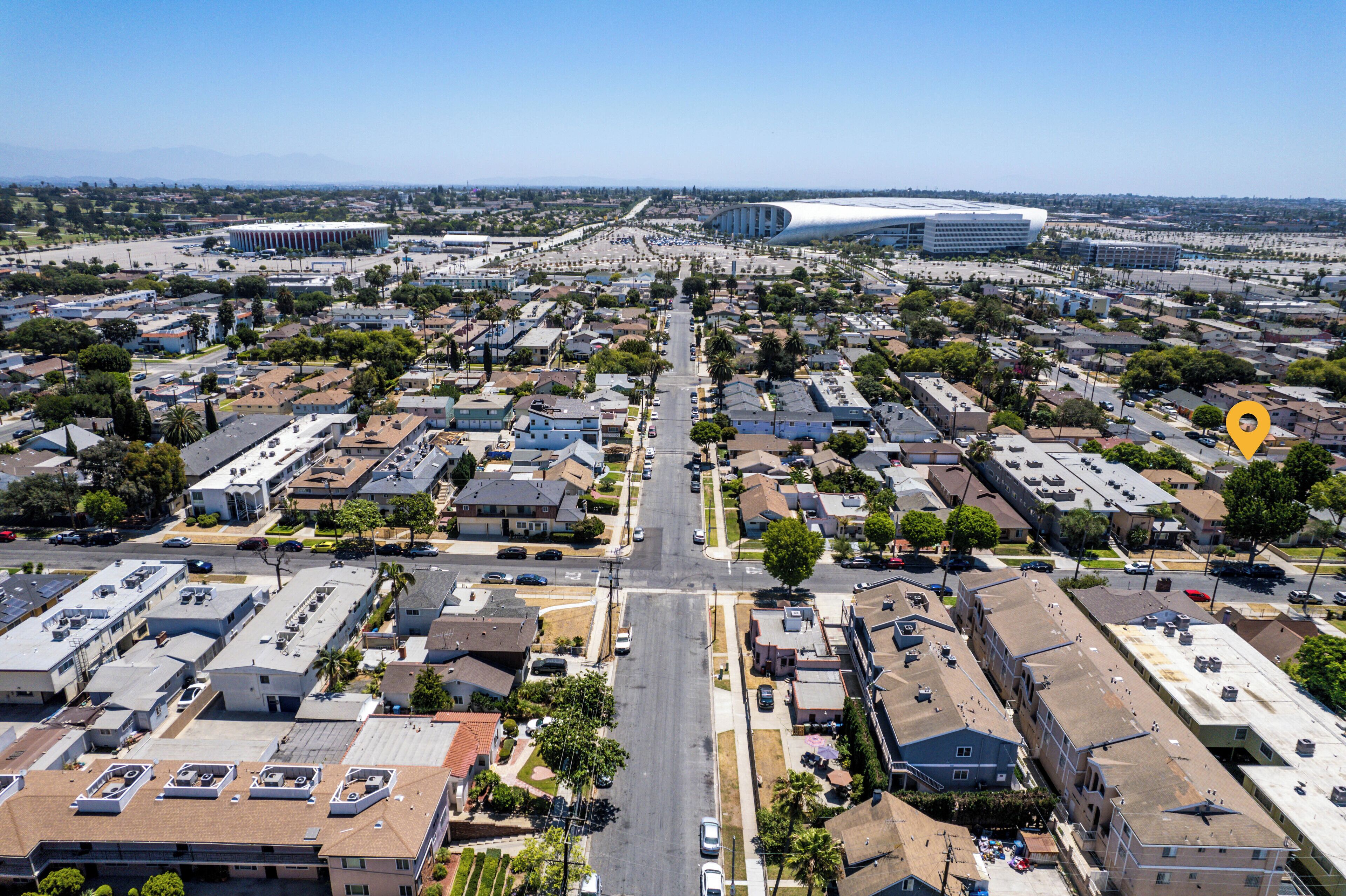 Vista aérea de una zona residencial con una avenida central, casas y un estadio grande al fondo.