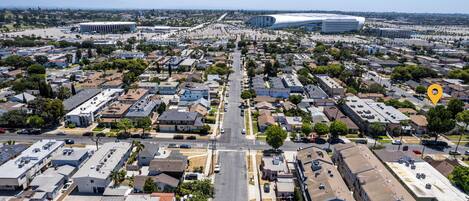 Vista aérea de una zona residencial con una avenida central, casas y un estadio grande al fondo.