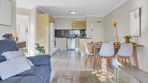 A modern living room with a grey sofa, a dining area with wooden chairs and a glass table, and a kitchen with stainless steel appliances. - Bright 2-bed With Private Balcony & Serene View (Brisbane)