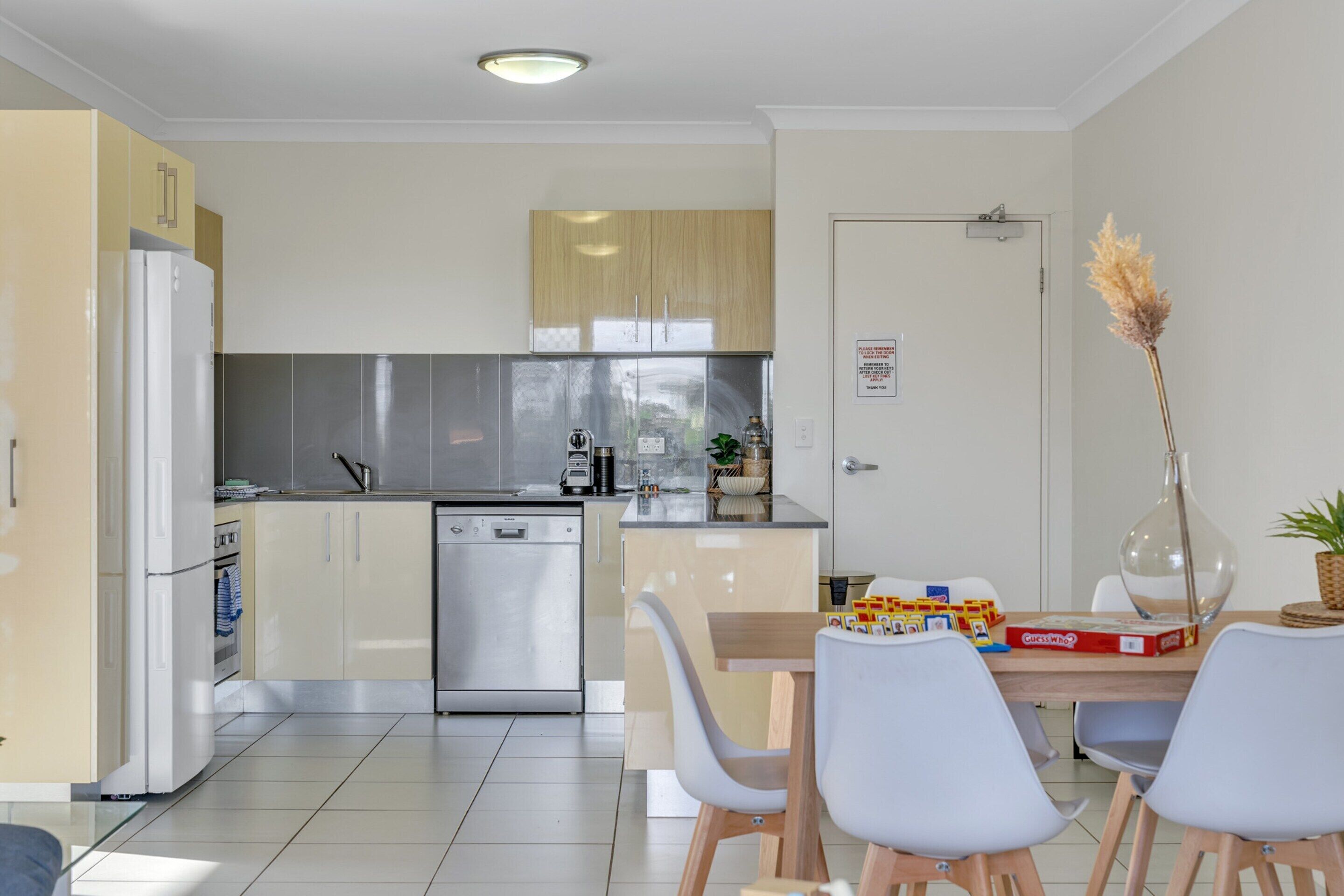 Een moderne keuken met een vaatwasser, een koelkast en een eethoek met een tafel en stoelen.