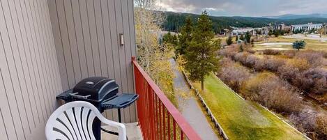 A balcony with a red railing, a white plastic chair, and a barbecue grill.