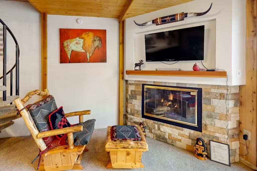 Una sala de estar acogedora con chimenea de piedra, televisor montado y un cuadro de un bisonte.