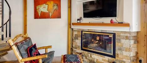 Una sala de estar acogedora con chimenea de piedra, televisor montado y un cuadro de un bisonte.