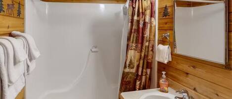 A wooden cabin bathroom with a shower, a sink, and a mirror.