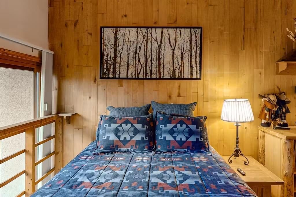Una stanza con pannelli di legno, un letto, cuscini, una lampada e un quadro appeso al muro.