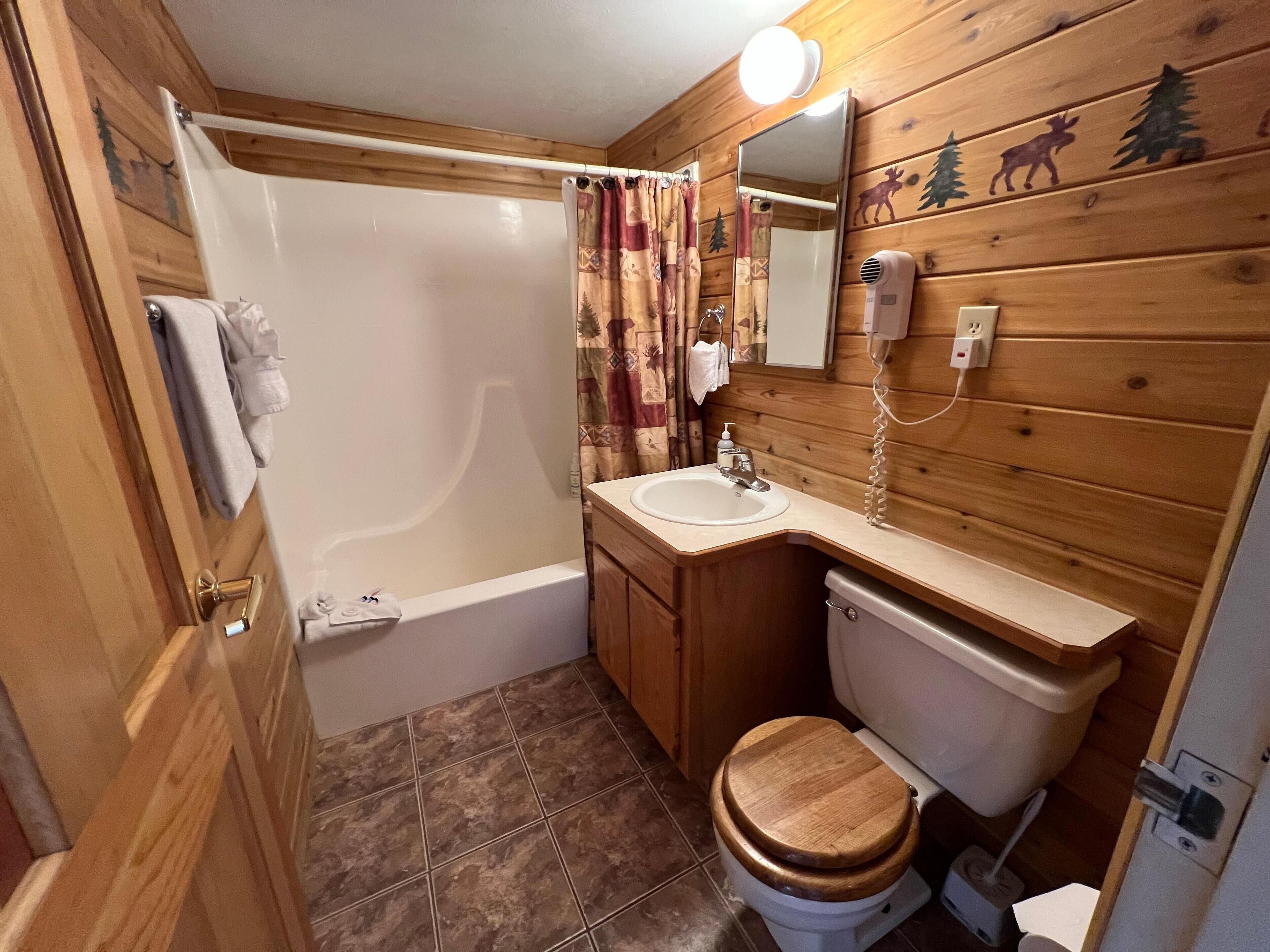 Baño de cabaña de madera con bañera, inodoro, lavabo y espejo.