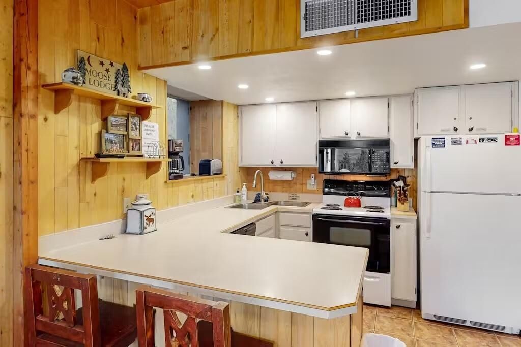 Una cocina con paredes de madera, armarios blancos, una isla central y un refrigerador.
