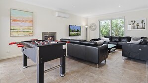 Een moderne woonkamer met een tafelvoetbalspel, een open haard, een bank en een groot raam.