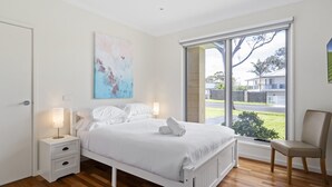 Een slaapkamer met een bed, nachtkastjes, een stoel, een raam en een schilderij aan de muur.