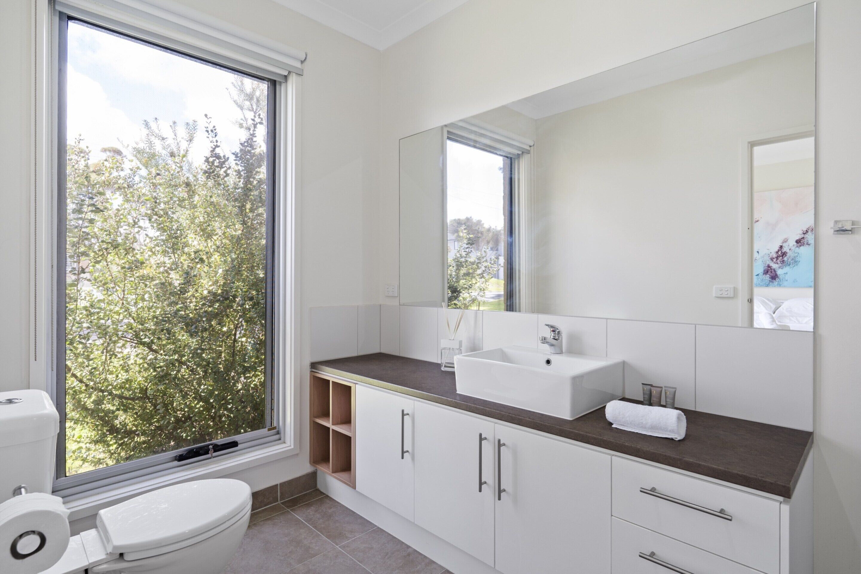 Un baño moderno con un ventanal grande, un lavabo blanco y un inodoro.