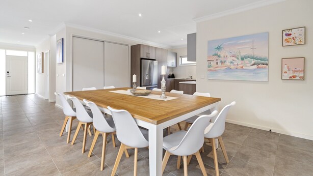 Een moderne keuken met witte kasten, een roestvrijstalen koelkast en een eethoek met een houten tafel en witte stoelen.