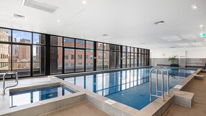 A modern indoor swimming pool with clear views of the cityscape through large windows. - Spacious Apartment in Heart of Southbank (Melbourne)