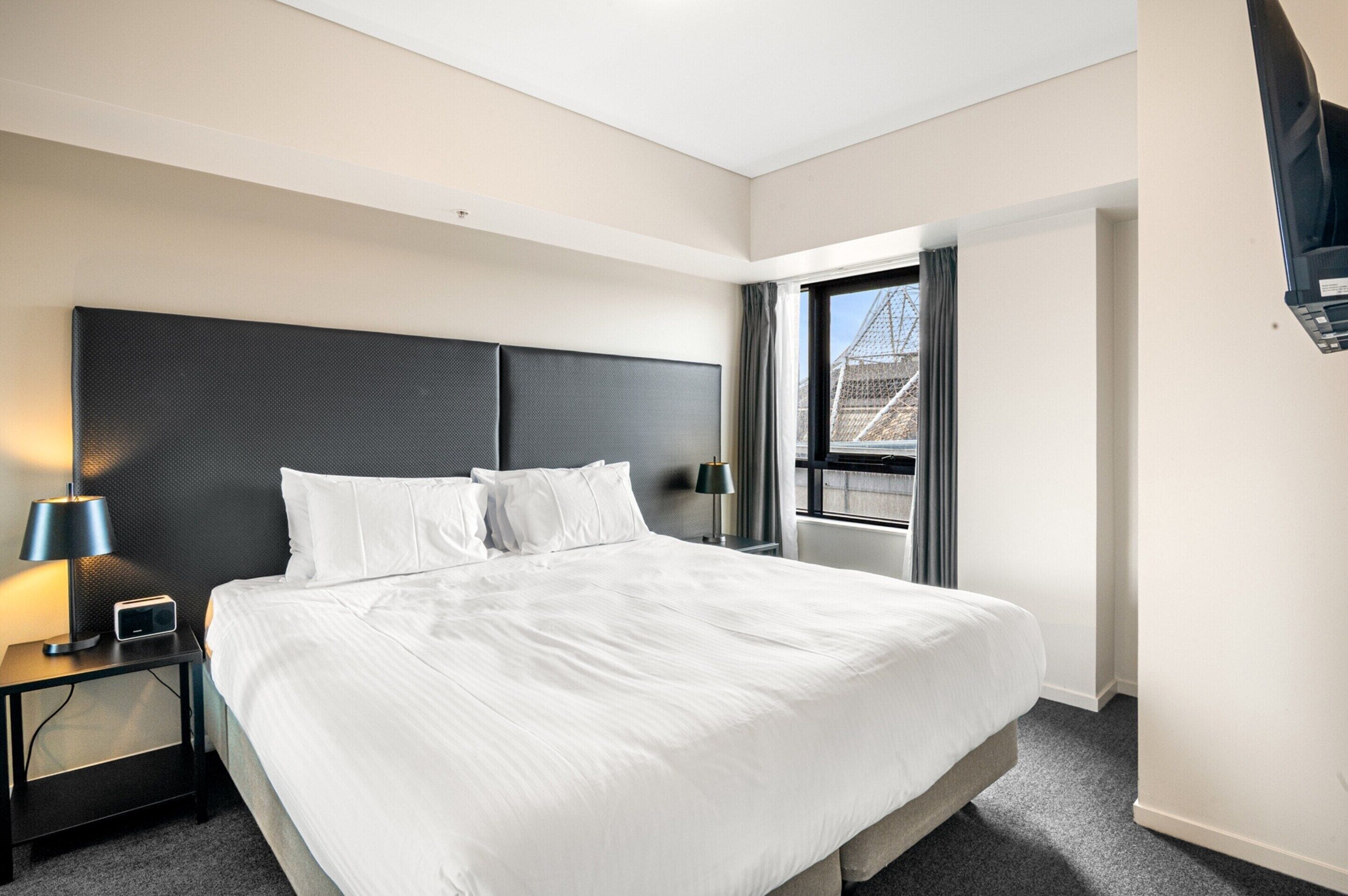 Et moderne hotelværelse med en stor seng, et natbord med en lampe og et vindue med gardiner.