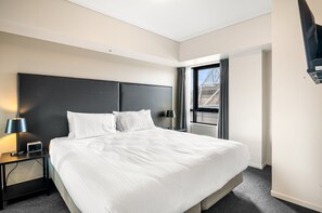 Una habitación de hotel moderna con una cama grande, una mesita de noche con lámpara y una ventana con cortinas.