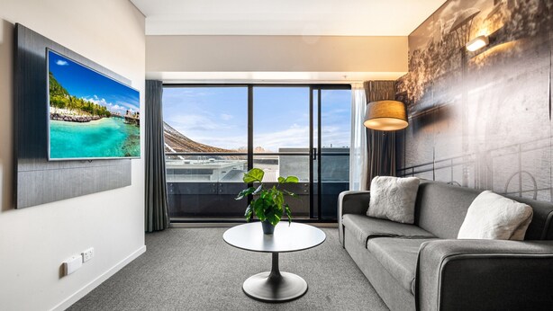 A modern living room with a flat-screen TV, a round coffee table, a grey sofa, and a large window with a view of a cityscape. - Spacious Apartment in Heart of Southbank (Melbourne)