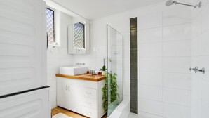 Een moderne badkamer met een douchecabine van glas, een wastafel met houten blad en een vloer van witte tegels.