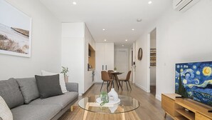 Una sala de estar moderna con una mesa de centro de vidrio, un sofá gris y un cuadro de un paisaje.