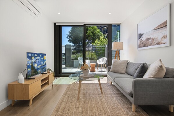 Un salon moderne avec un canapé gris, une table basse en verre, une console en bois et un tableau accroché au mur.