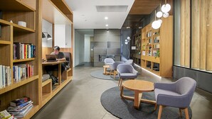 Una biblioteca moderna con estanterías, una persona usando una computadora portátil y un área de descanso con mesas y sillas.