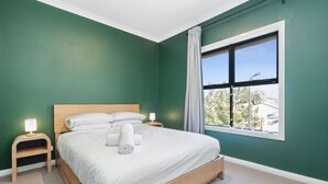 A neatly made bed with white linens and pillows, a bedside lamp, and a nightstand. - Bright 2-bed Townhouse With Balcony & Garage (Adelaide)