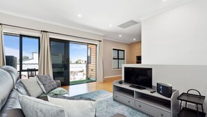 A modern living room with a sofa, TV, and entertainment unit. - Bright 2-bed Townhouse With Balcony & Garage (Adelaide)