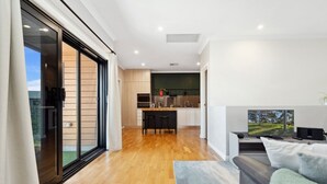 A modern kitchen with a dining area, a living room with a sofa, and a large sliding glass door leading to an outdoor area. - Bright 2-bed Townhouse With Balcony & Garage (Adelaide)